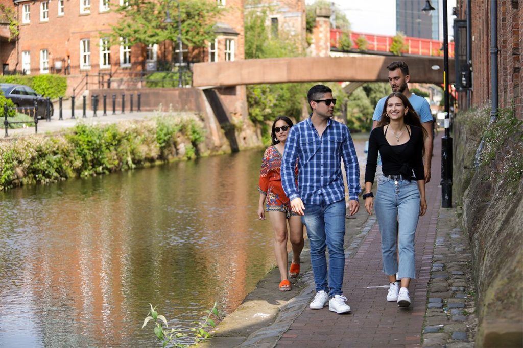 Students walking along a canal in sunny Manchester