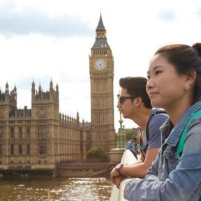 Two students lean over a bridge with Big Ben and the houses of parliament in the background
