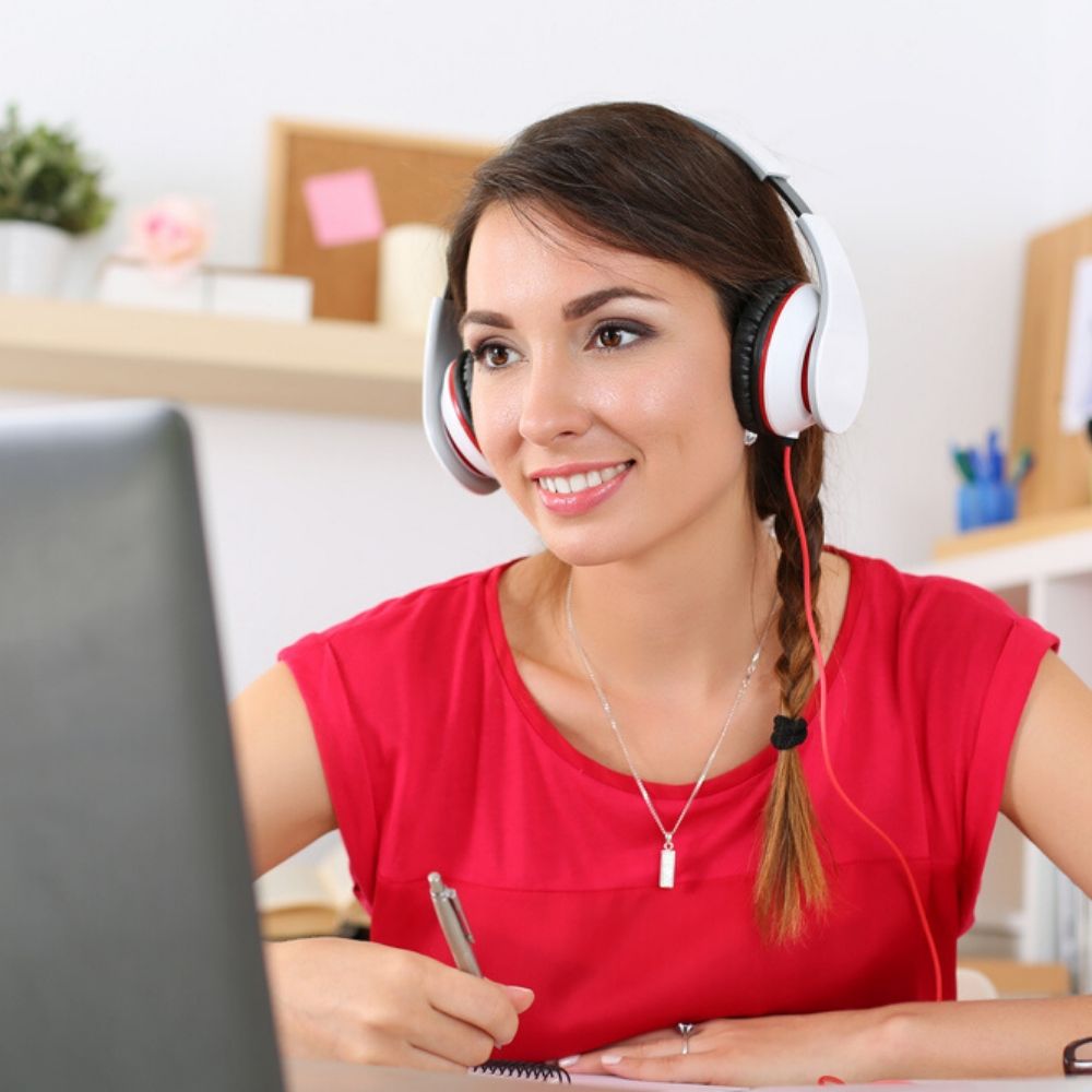Girl in red top with headphones and laptop prepares for IELTS exam