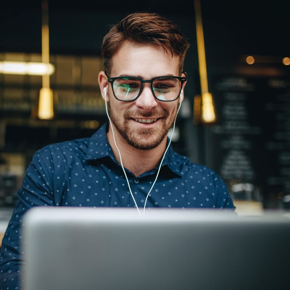 Man wearing glasses using laptop and earphones