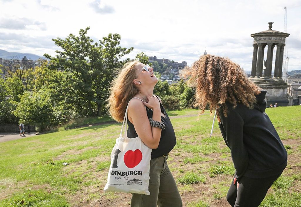 Students laughing in a park, holding an Edinburgh bag.