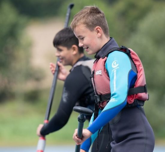 Two boys smiling, wearing life vests and wetsuits